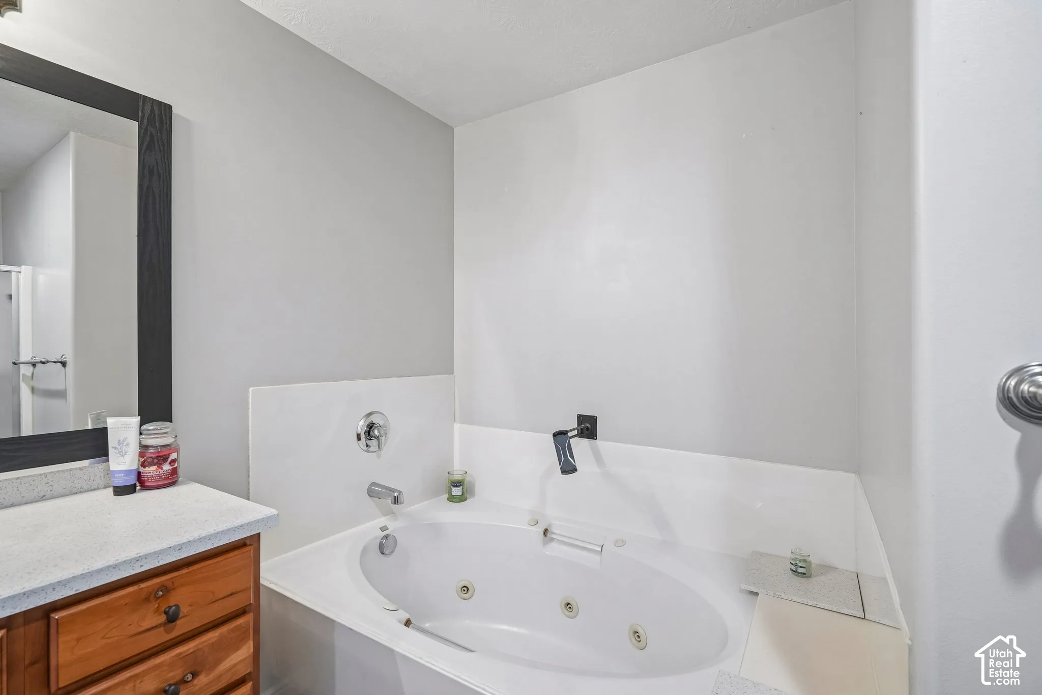 Oval jetted soaking tub with a wall-mounted faucet, wood-finish vanity cabinet, solid surface countertop, and framed mirror