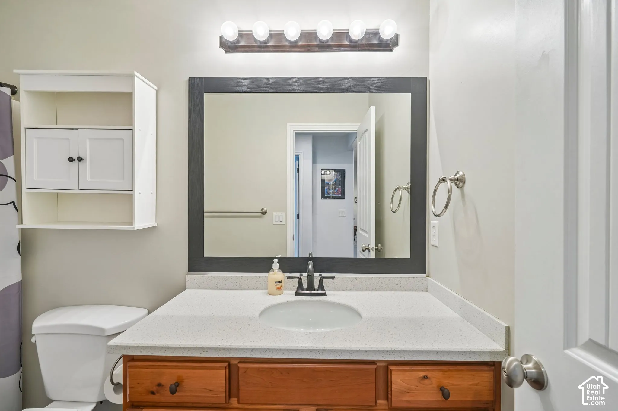 Bathroom vanity featuring a speckled composite countertop, undermount sink, dark-finish faucet, framed mirror, and wall-mounted storage cabinetry