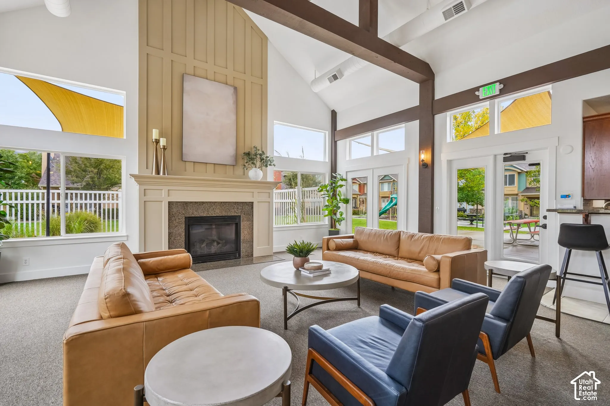 Vaulted ceilings featuring exposed timber beams, expansive windows with transoms, floor-to-ceiling fireplace surround with millwork detailing, and full-glass panel doors
