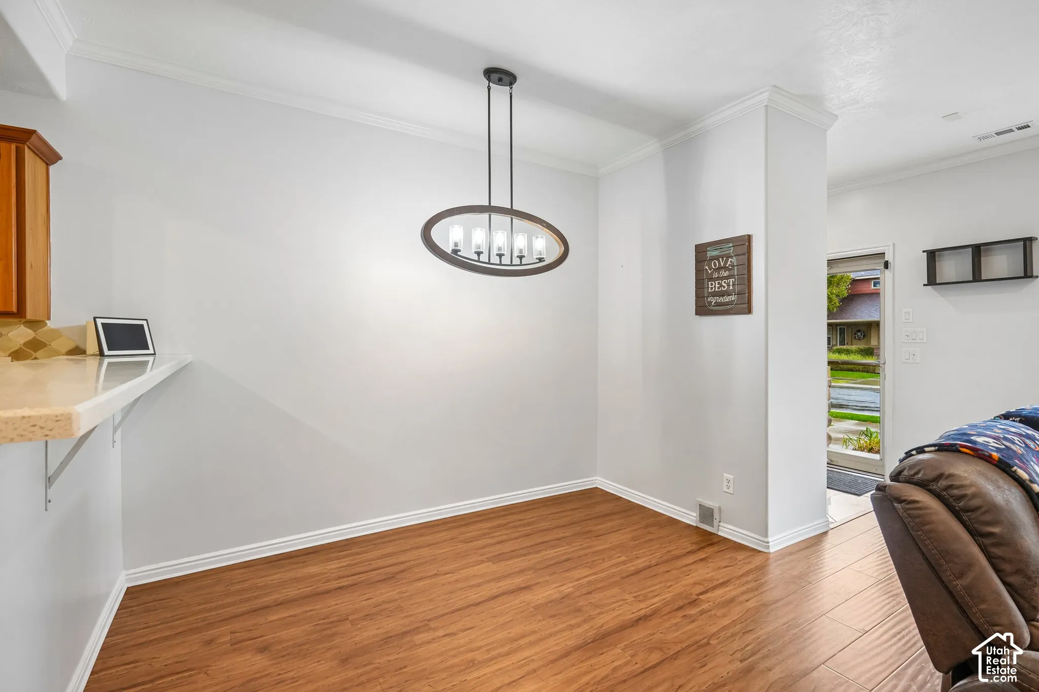 Oval multi-light chandelier, wood-finish flooring, and crown molding