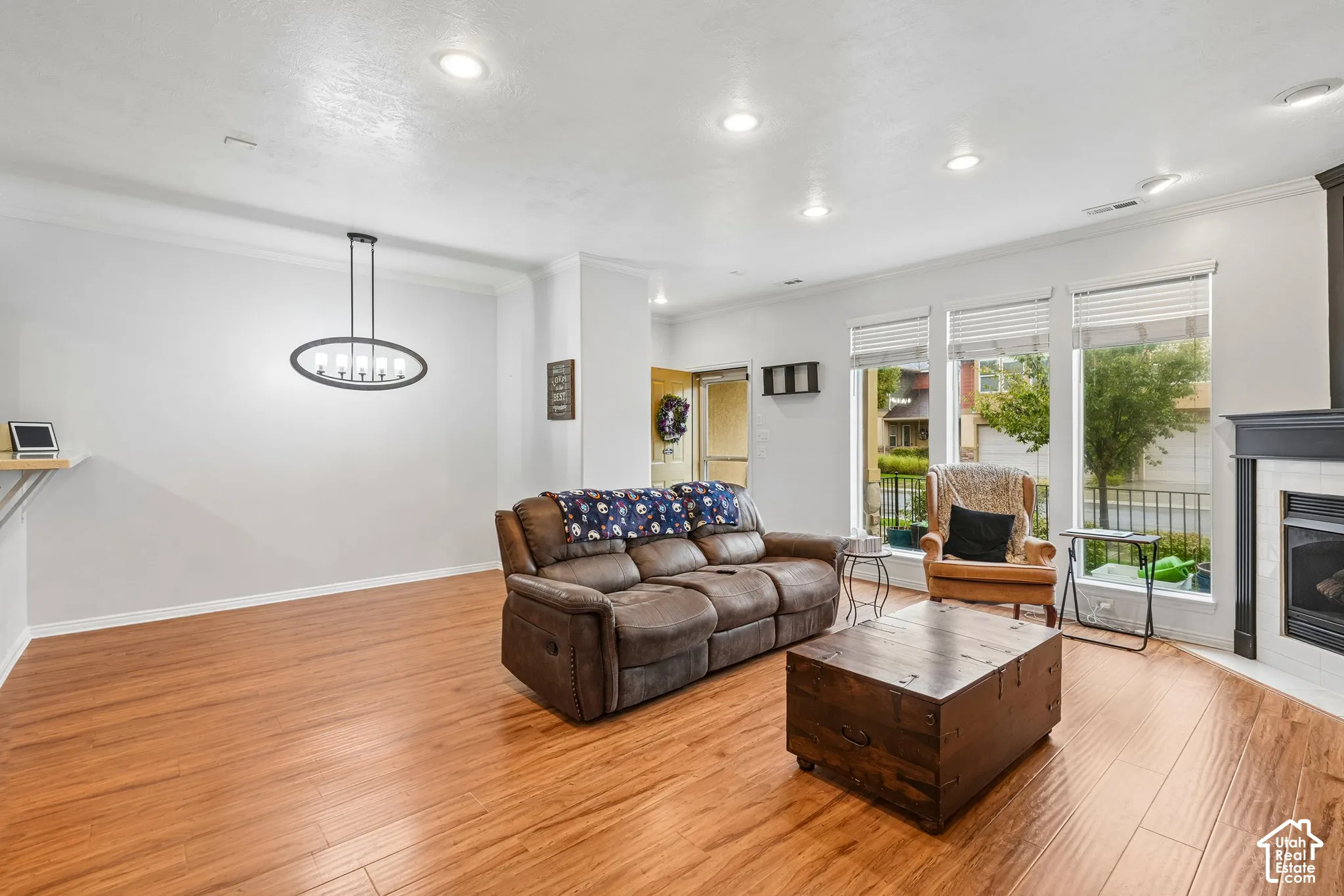 Living area featuring wood-finish flooring, recessed lighting, a modern oval-style chandelier, and a fireplace with a dark mantle surround