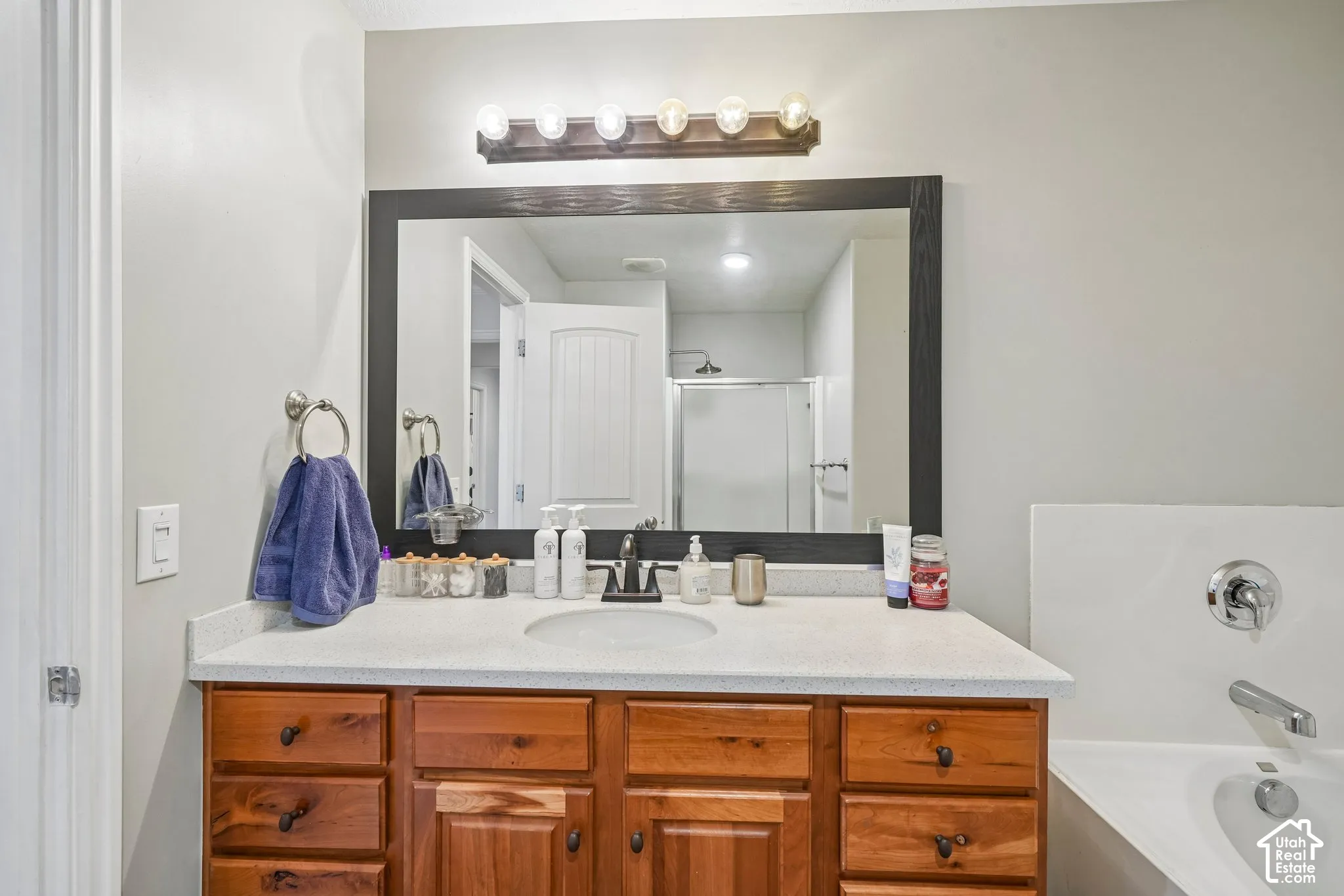 Bathroom vanity featuring a light-toned solid surface countertop, undermount sink with a dark finish faucet, medium-tone wood cabinetry, a large framed wall mirror, and a multi-bulb vanity light fixture