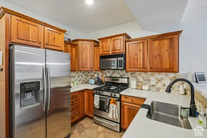 Kitchen featuring wood cabinetry, stainless steel appliances, neutral stone-finish countertops, diamond-patterned tile backsplash, and a matte black gooseneck faucet