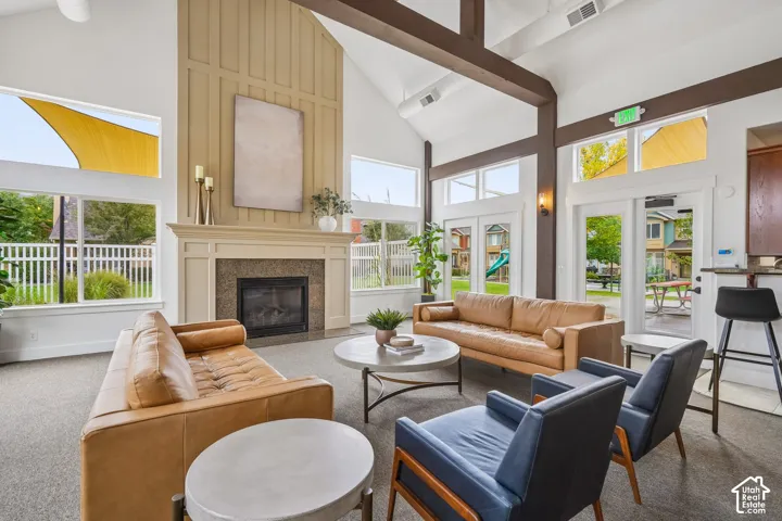 Vaulted ceilings featuring exposed timber beams, expansive windows with transoms, floor-to-ceiling fireplace surround with millwork detailing, and full-glass panel doors