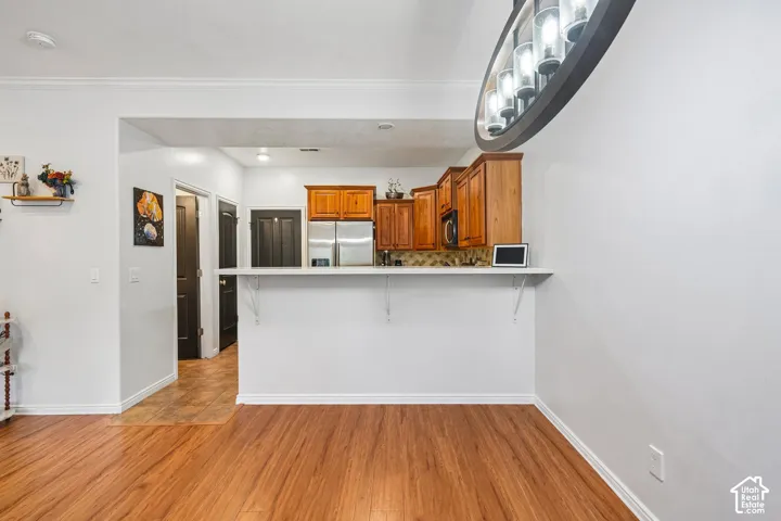 Kitchen featuring wood cabinetry, a white breakfast bar, patterned backsplash, wood-finish flooring, and a circular multi-bulb pendant fixture