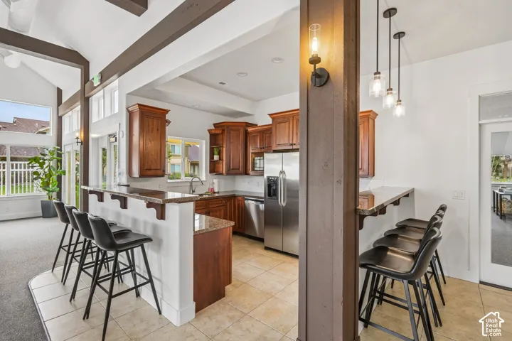 Kitchen featuring wood cabinetry, stone countertops, stainless steel appliances, tile flooring, and vaulted ceilings with exposed wood beams