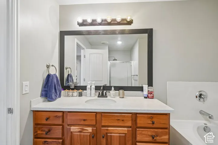 Bathroom vanity featuring a light-toned solid surface countertop, undermount sink with a dark finish faucet, medium-tone wood cabinetry, a large framed wall mirror, and a multi-bulb vanity light fixture
