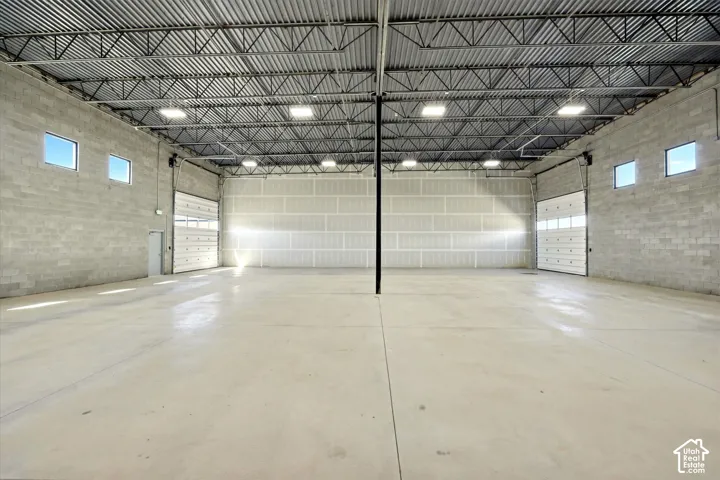 Expansive warehouse space featuring concrete block walls, exposed metal truss ceiling, polished concrete flooring, multiple overhead doors, and natural light from transom windows