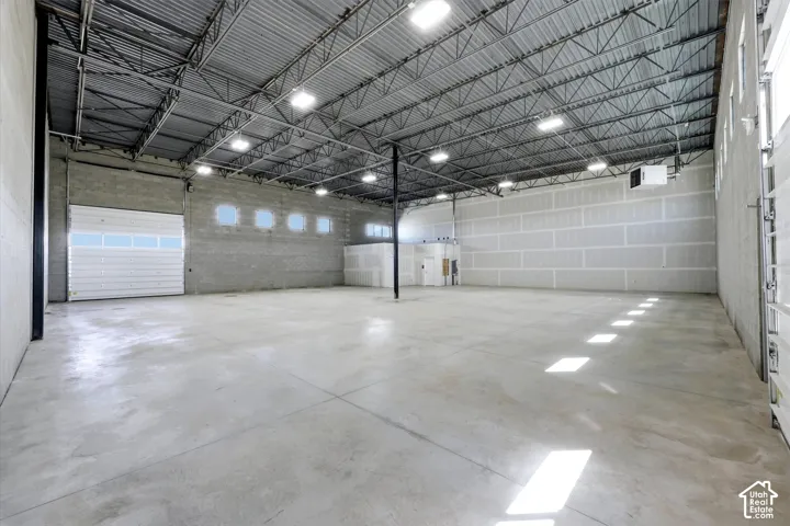 Spacious industrial interior featuring a high corrugated metal ceiling, exposed metal trusses, concrete block walls, a large roll-up door, and polished concrete flooring