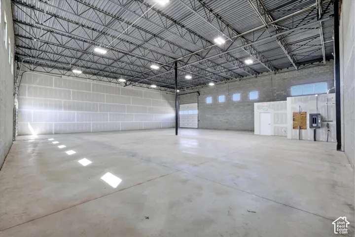 Spacious interior featuring a concrete floor, exposed metal ceiling trusses, multiple overhead light fixtures, and an overhead door