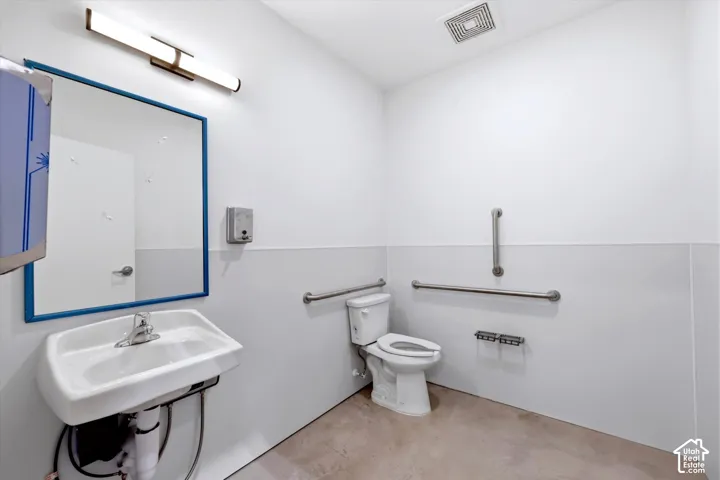 White walls with a light gray wainscoting, wall-mounted sink, and a toilet with grab bars