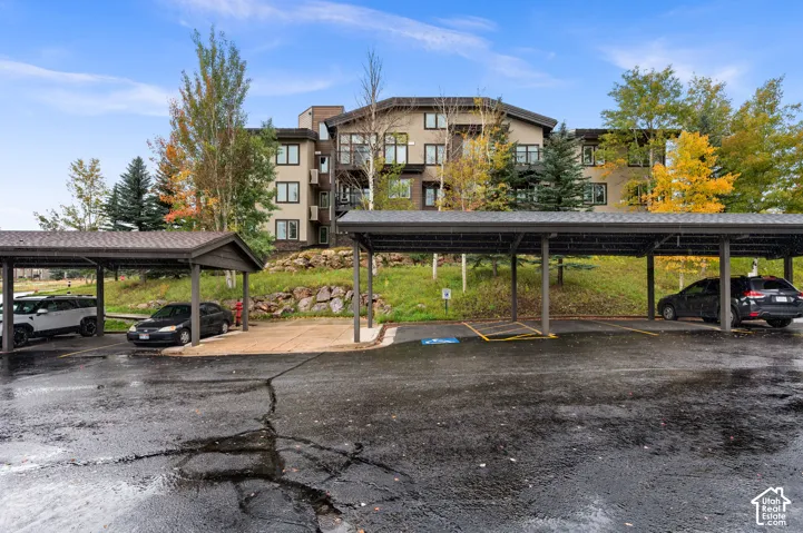 Multi-story residential building exterior featuring a contemporary facade, shingle roofing, sheltered carport structures, and landscaped rock embankment