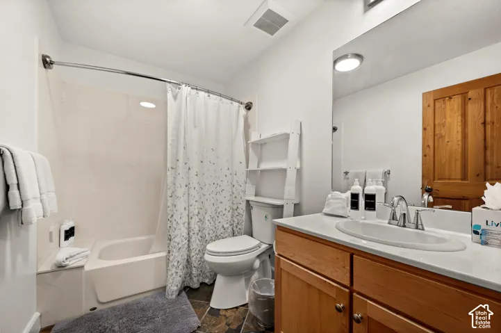 Bathroom featuring a wooden vanity with a stone countertop, an integrated sink, a full-width vanity mirror, and a shower-tub combination with a paneled surround