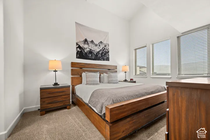 Vaulted ceiling, neutral wall-to-wall carpeting, and triple windows featuring horizontal blinds