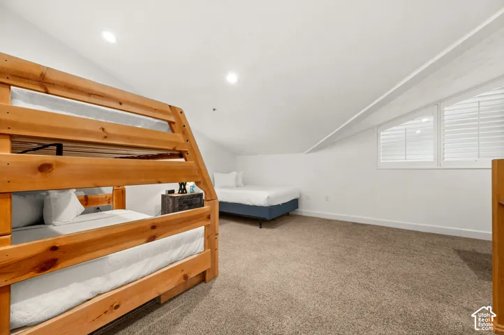 Spacious room featuring a vaulted ceiling, wall-to-wall carpeting, and angled windows with interior shutters