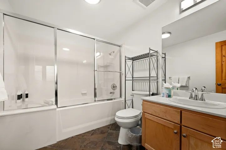 Bathroom featuring a tub-shower combination with sliding glass doors, vanity with stone-style countertop and integrated sink, and stone-finish floor tiling