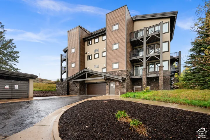 Multi-story exterior featuring stone veneer siding, horizontal wood-finish cladding, private balconies with metal railings, and a covered garage entrance