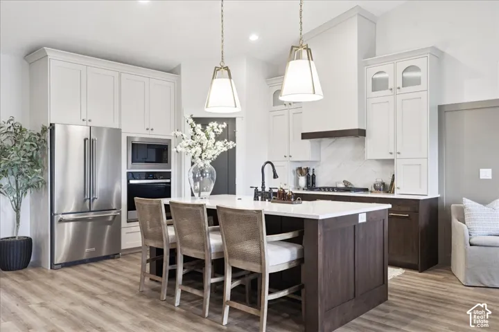 Kitchen featuring contrasting cabinetry, stone-surface island with integrated sink, stainless steel built-in oven and microwave, stone-look backsplash, and wood-finish flooring