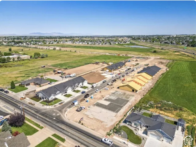 Aerial perspective of a developing residential community featuring paved roads, concrete foundations, and multi-unit construction with dark-toned shingle roofing