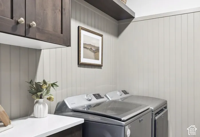 Laundry area featuring dark-stained wood cabinetry, white stone-finish countertop, beadboard wall paneling, and an overhead wooden shelf