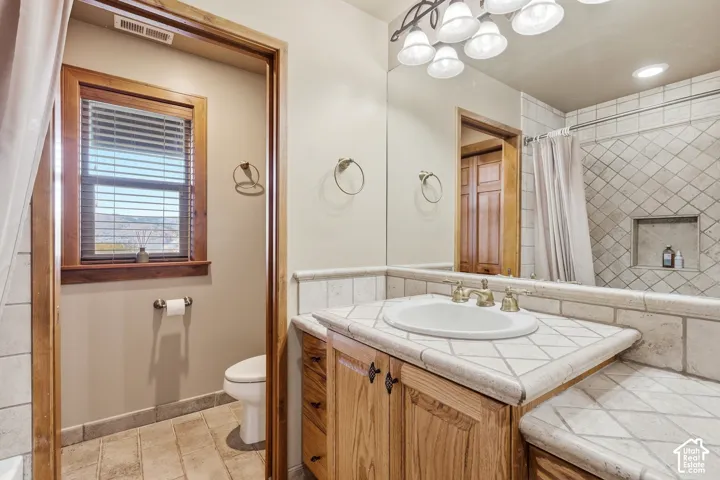 Bathroom featuring a custom tile-topped vanity with an integrated basin, natural-finish wood cabinetry, a tiled shower surround with a built-in recessed niche, and stone-tile flooring
