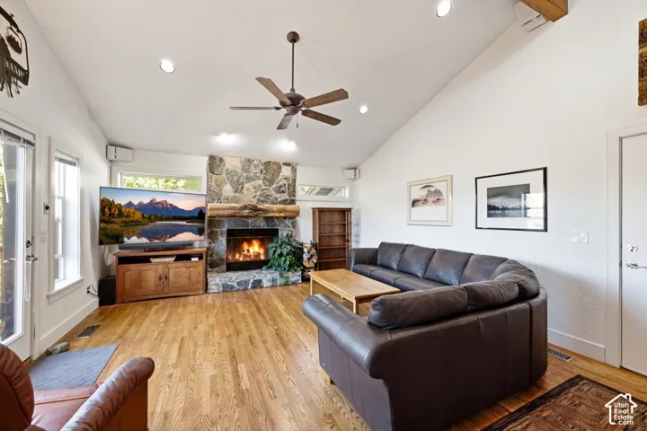 Vaulted ceiling featuring recessed lighting, floor-to-ceiling natural stone fireplace with timber mantel, and wood-finish flooring
