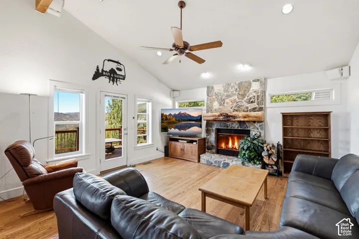 Vaulted ceilings featuring a ceiling fan, stone-surround fireplace with a rustic timber mantel, wood-finish flooring, built-in shelving, and multiple windows providing natural light
