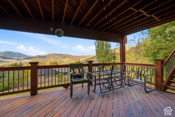 Covered wood deck featuring a protective roof structure, dark-finish metal balusters, integrated staircase, and panoramic mountain scenery