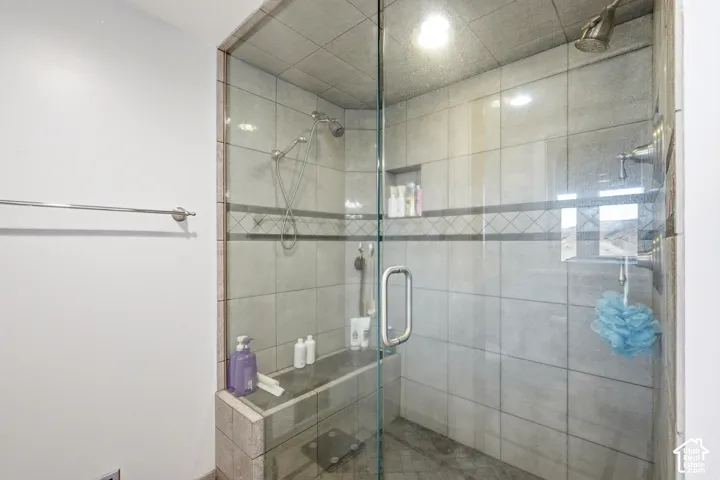Walk-in shower featuring a frameless glass door, built-in tile bench, dual shower heads, integrated wall niche, and decorative tile inlay