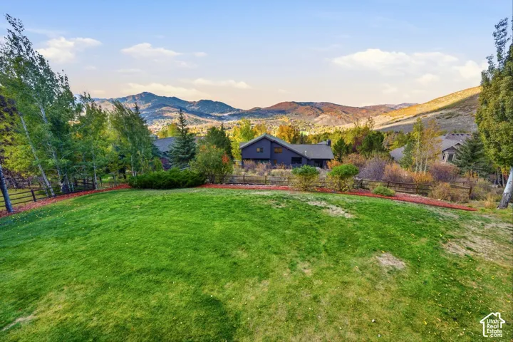 Expansive lawn with mature trees, split-rail fencing, and prominent mountain backdrop