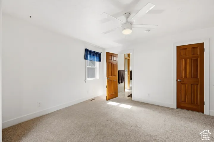 Interior space featuring wall-to-wall carpeting, neutral-toned walls, six-panel wood-finish doors, and a multi-blade ceiling fan with integrated light fixture