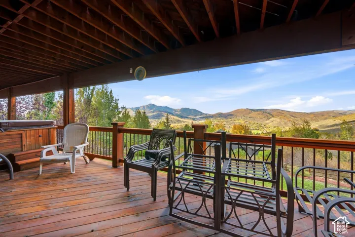 Covered deck featuring wood-finish flooring, built-in hot tub, and railings with metal balusters, overlooking a mountain landscape