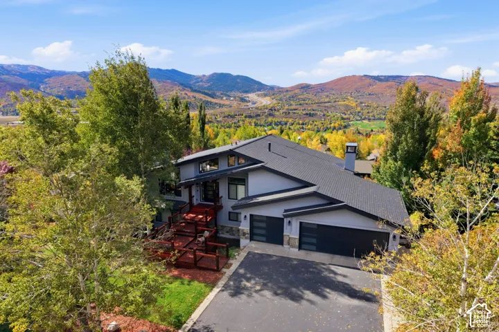 Multi-level exterior featuring a combination of light-toned siding and stone masonry, asphalt shingle roof, multi-car garage with horizontal glass paneling, and elevated wood-finished decking