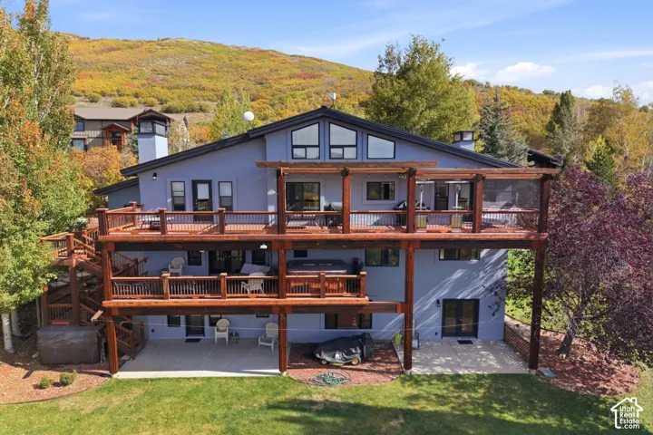 Multi-level residence featuring expansive tiered wooden decks, heavy timber framing, integrated hot tub, and large angular windows against a mountain backdrop