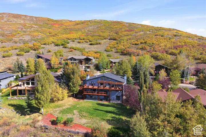 Multi-level residence featuring stacked wood-railing decks, heavy timber pergola detailing, stone chimney elements, and an expansive lawn set against a mountain hillside