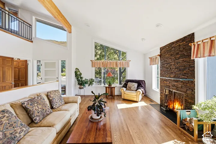 Vaulted ceiling with exposed wood beam, stacked stone fireplace, floor-to-ceiling multi-pane windows, and wood-finish flooring