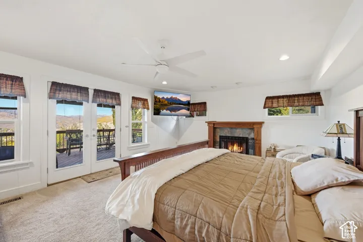 Fireplace with a wood mantle and stone surround, double glass-pane doors leading to an outdoor deck, mountain backdrop, and ceiling fan