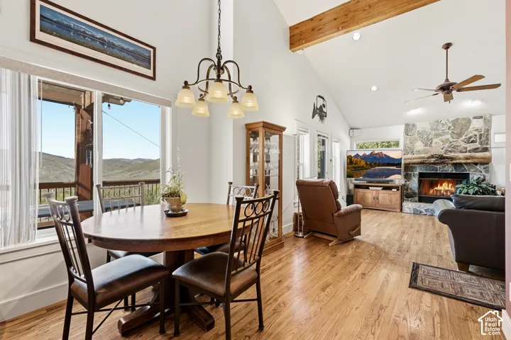 Vaulted ceilings featuring exposed timber beams, wood-finish flooring, and floor-to-ceiling stone fireplace with a natural log mantel
