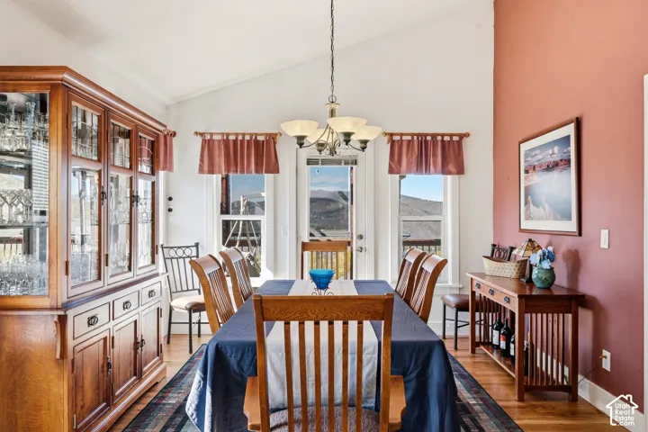 Dining area featuring vaulted ceilings, wood-finish flooring, a multi-bulb chandelier, and large windows with mountain scenery