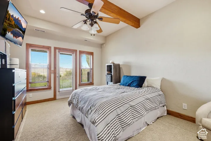 Vaulted ceiling featuring an exposed wood beam, ceiling fan with integrated lighting, neutral wall-to-wall carpeting, and double-pane windows with wood trim