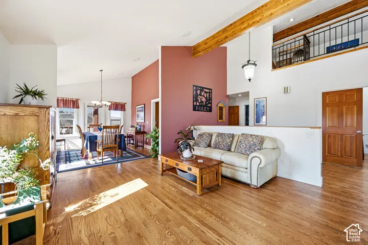 Open-concept interior featuring wood-finish flooring, vaulted ceilings with exposed wood beams, and an elevated mezzanine with metal railing