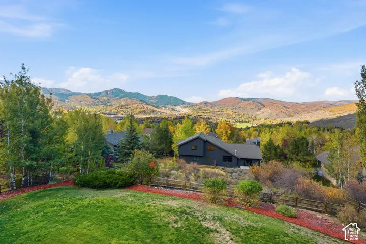 Elevated lot featuring a grass lawn, decorative red mulch border, split-rail wood fencing, and expansive mountain scenery