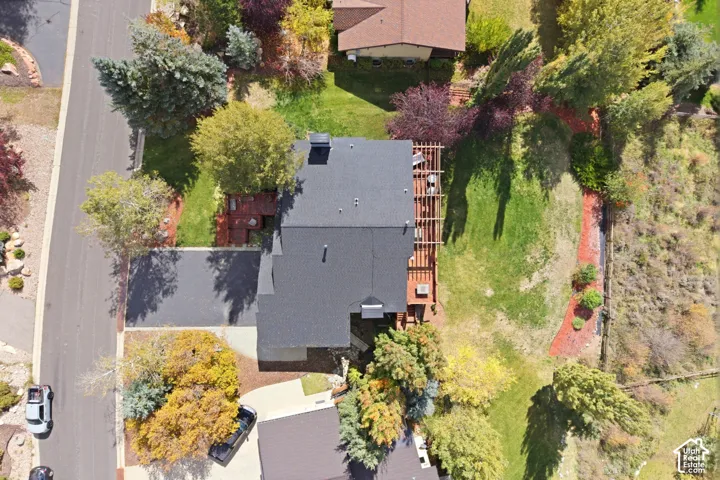 Aerial perspective of a property featuring an asphalt driveway, wood-framed rear deck, mature landscaping, and expansive lawn area