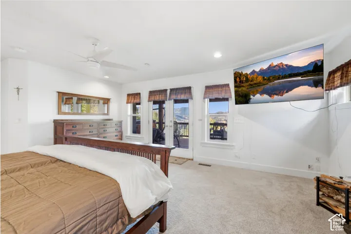 Carpeted room featuring a ceiling fan, multiple windows, and a glass-paneled door with mountain scenery