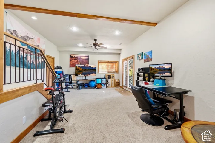 Open-concept interior featuring exposed wooden ceiling beams, recessed lighting, carpeted flooring, and a metal stair railing with a wood cap