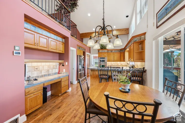 Vaulted ceilings with exposed timber beams, wood-finish flooring, custom oak cabinetry, built-in desk workstation, and decorative tile backsplash