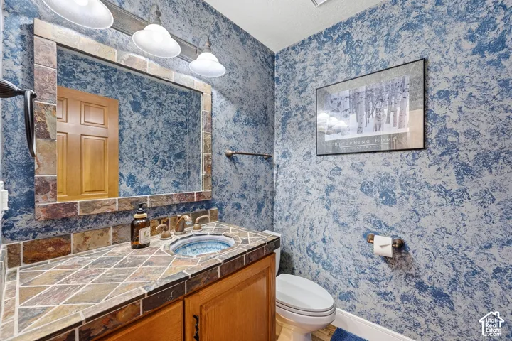Stone-tiled vanity countertop featuring an integrated vessel sink, framed mirror with matching stone tile surround, multi-bulb wall-mounted vanity lighting, and textured wall finish