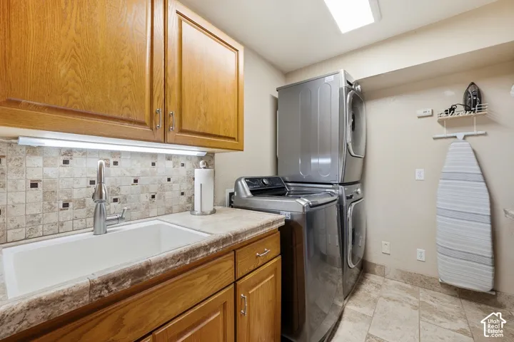 Laundry area featuring wood-finish cabinetry, tile backsplash, undermount sink with chrome-finish faucet, and stone-finish countertop