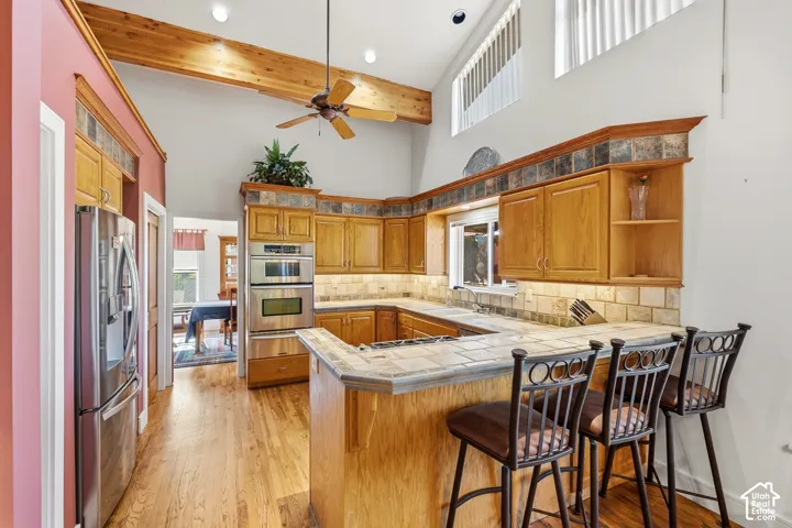 Kitchen featuring vaulted ceilings with exposed wood beams, wood-finish cabinetry, tile countertops, built-in double wall ovens, and wood-finish flooring