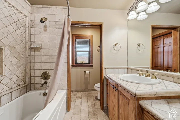 Bathroom featuring tiled shower surround with diagonal inlay, custom wood cabinetry, stone-topped vanity with an integrated oval sink, and multi-bulb decorative light fixture